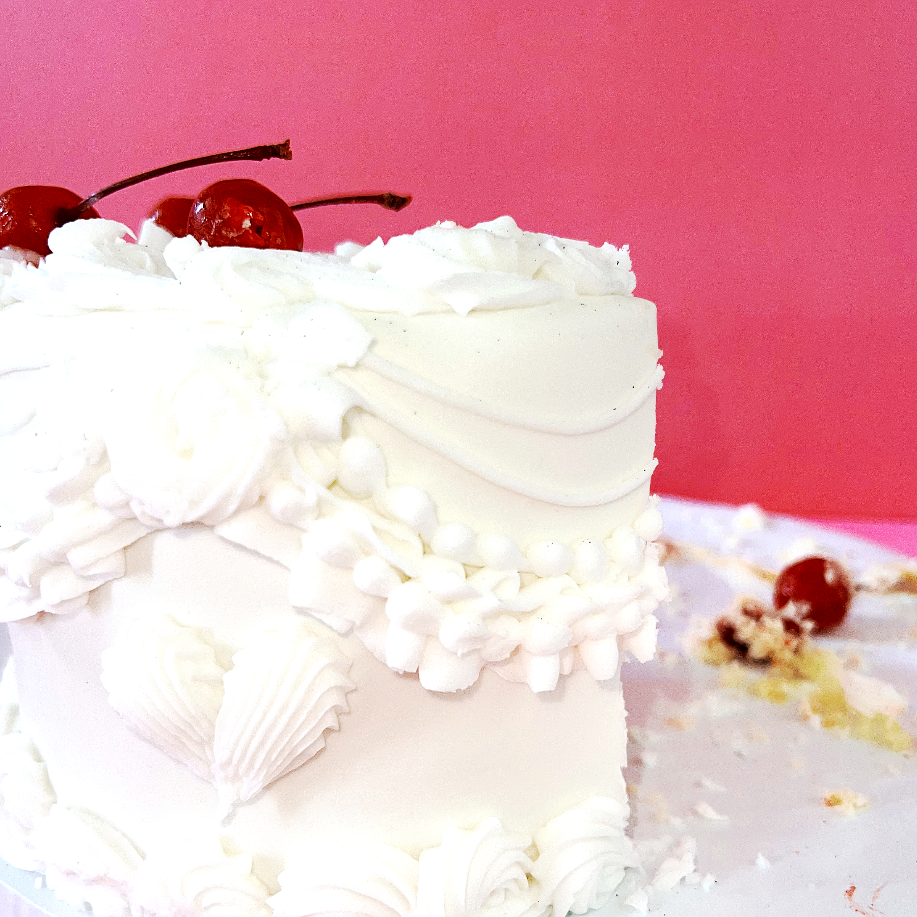 A close up of a yummy cake with vintage white piping on the outside and red cherries all round.
