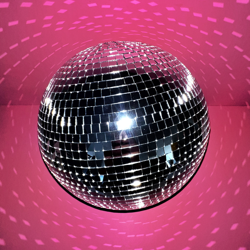 A sparkly disco ball shining on a pink backdrop.